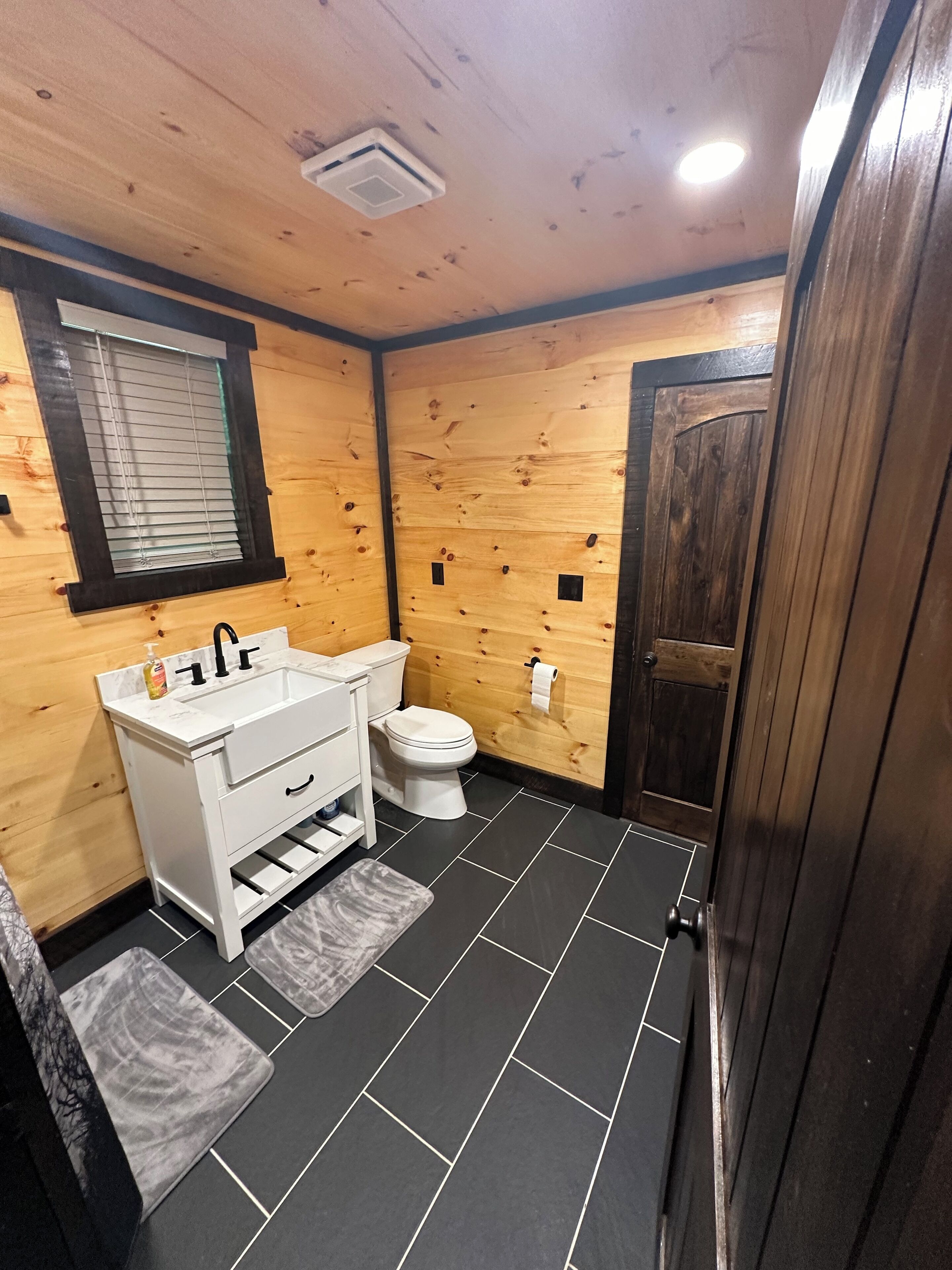 A compact bathroom with a white sink, toilet, and wooden walls.