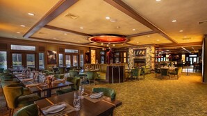 Un restaurant spacieux avec de longues tables, des chaises recouvertes d’un tissu vert et un tapis à motifs.