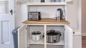Eine kompakte Küche mit weißen Schränken, einer Holz Arbeitsplatte und verschiedenen Geräten, darunter ein Toaster, ein Wasserkocher und ein Slow-Cooker.