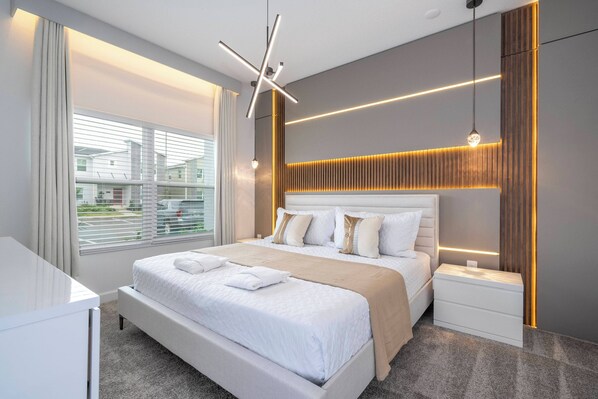 A modern hotel room with a large bed, bedside tables, a desk, and a view of the outside.