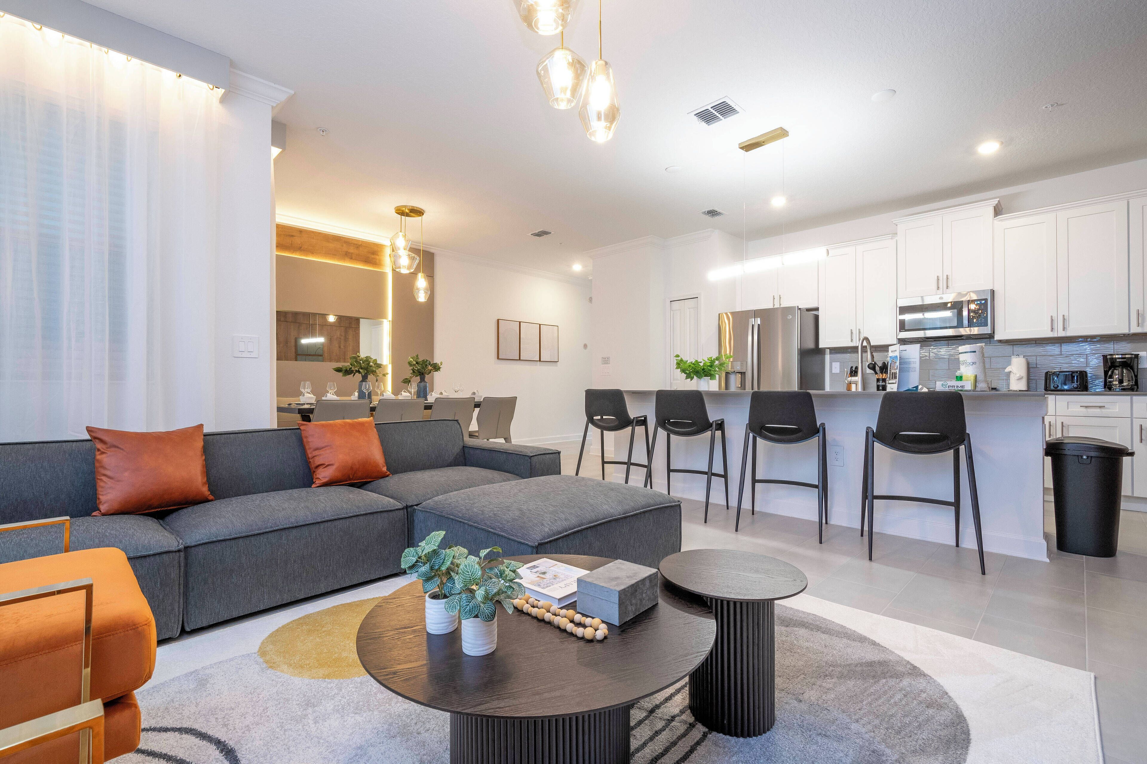 A modern living room with a grey sectional sofa, a round coffee table, and a dining area with bar stools.