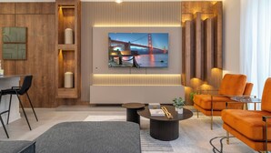 Ein modernes Wohnzimmer mit großem Fernseher, der eine Brücke zeigt, einer Couch, einem Couchtisch und einem Essbereich mit Stühlen.