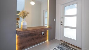 Ein Empfangsschalter mit Holzoptik, eine Blumenvase und ein großer Spiegel darüber, sowie eine Tür mit Fenster.
