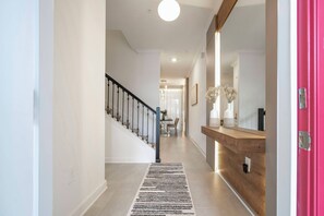 A hallway with a wooden floor, a black and white rug, a staircase with a black railing, and a wooden console table with a mirror.