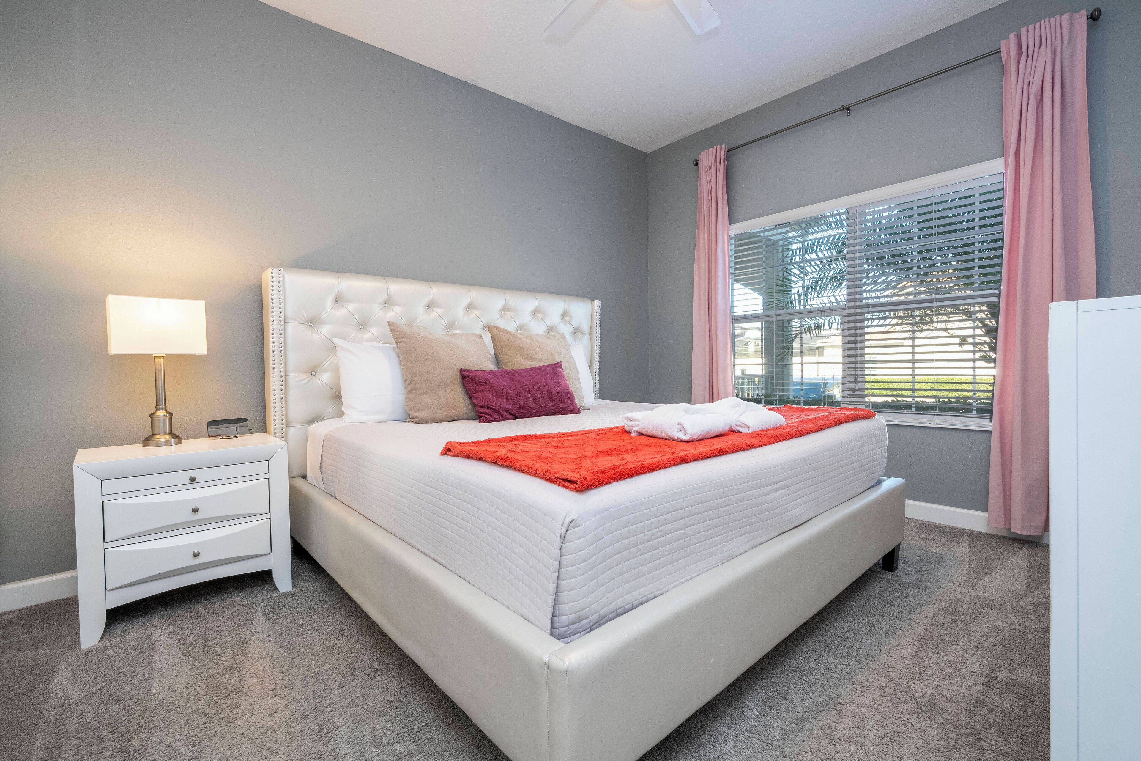 Een keurig opgemaakt slaapkamer met een groot bed, een nachtkastje met lamp en een raam met gordijnen.