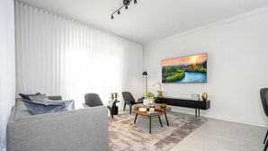 A modern living room with a grey sofa, a coffee table, and a painting of a landscape. - Private 4BR Check In and Chill Out (2417ST) (Kissimmee)