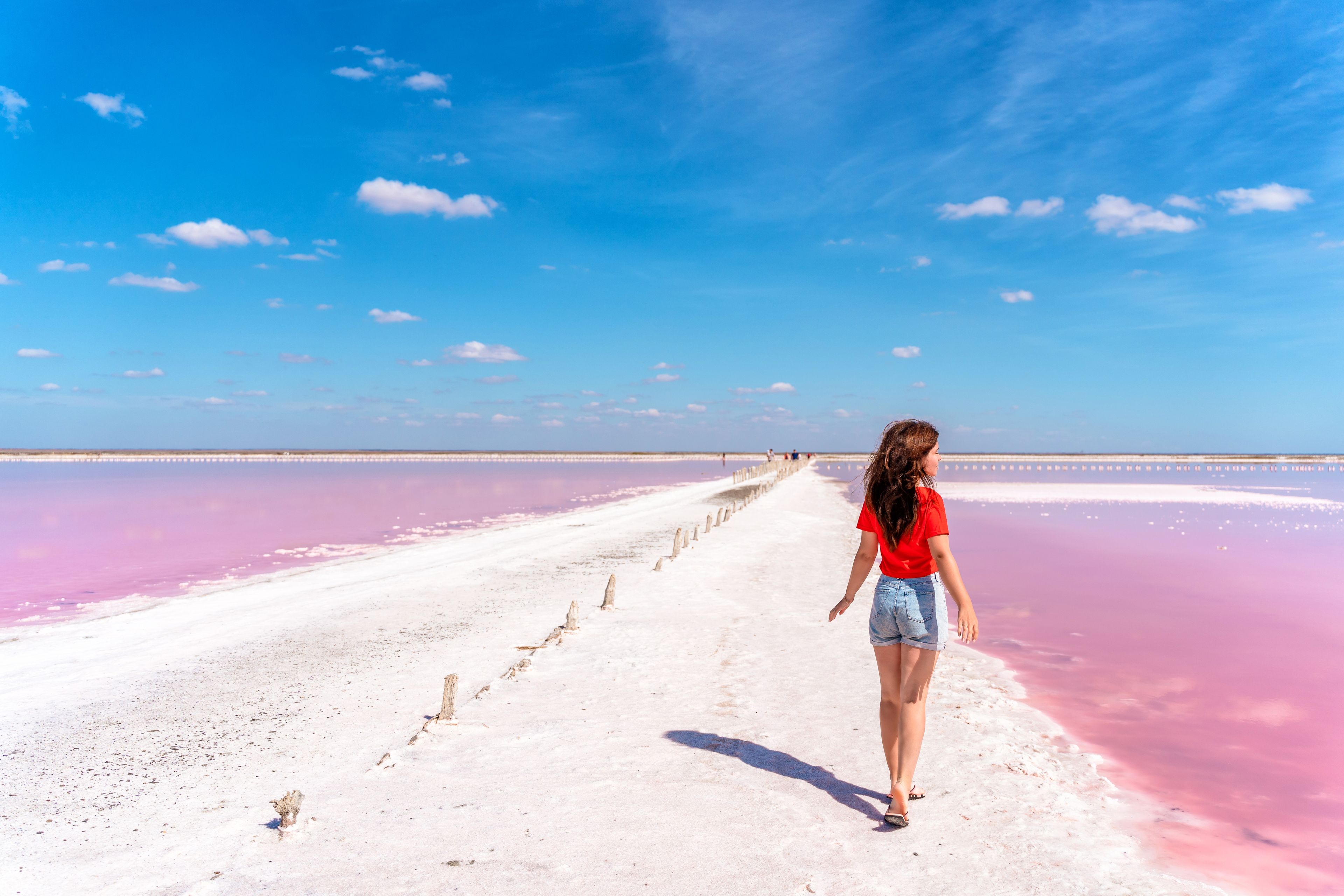 A person walking on a boardwalk with a pink and white beach in the background.