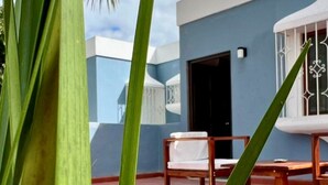Un balcón con una silla blanca y una mesa de madera, una pared azul y una puerta.