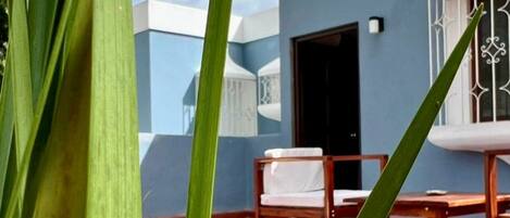 A balcony with a white chair and a wooden table, a blue wall, and a door.
