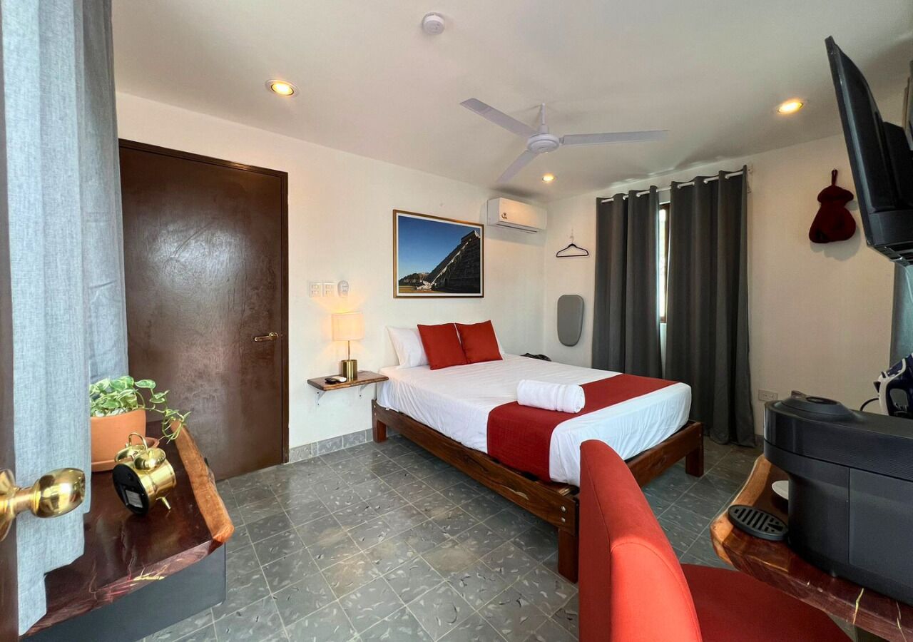Een hotelkamer met een bed, een televisie, een plafondventilator en een raam met gordijnen.