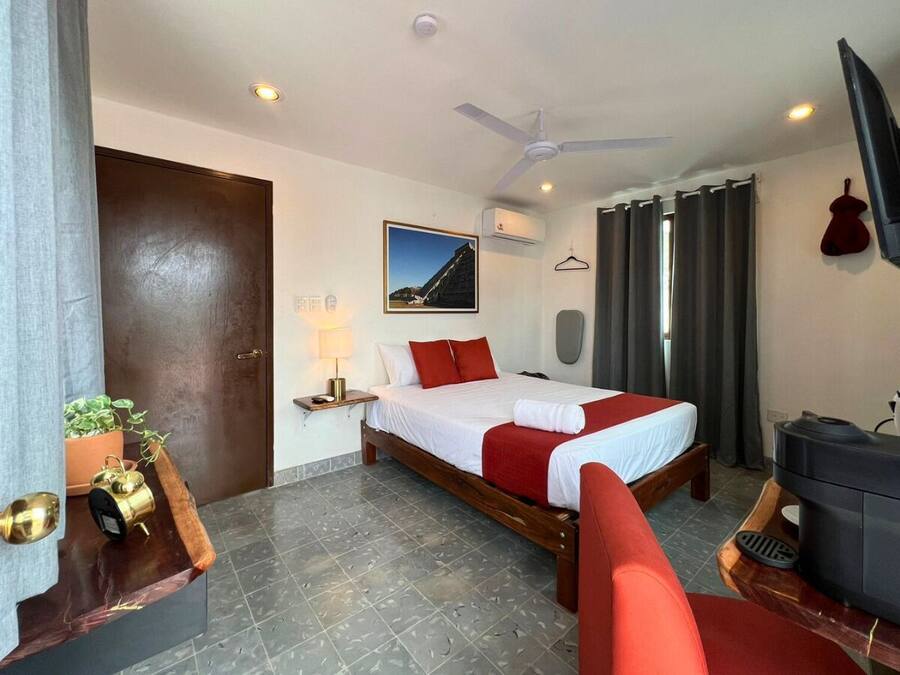 Een hotelkamer met een bed, een televisie, een plafondventilator en een raam met gordijnen.