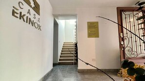 Un pasillo con una escalera que conduce a una plataforma, un cartel que dice "CASA EKINOX" y una puerta metálica decorativa.