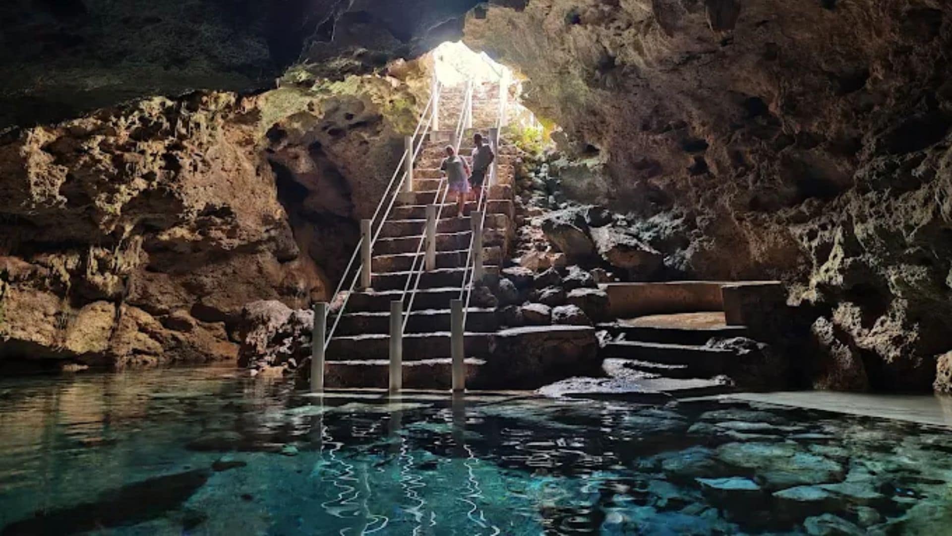 Une piscine à l’eau claire, entourée de murs rocheux, et un escalier menant à un niveau supérieur.