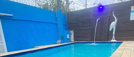 Una piscina con cercado azul, una estatua blanca y una escalera de metal.