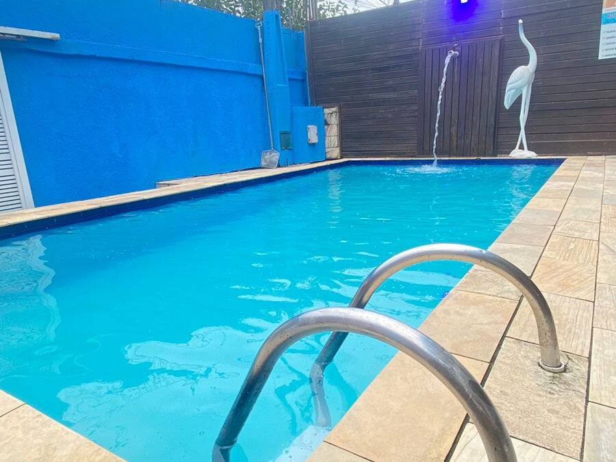 Una piscina con cercado azul, una estatua blanca y una escalera de metal.
