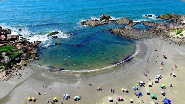 Une plage avec une eau cristalline, des formations rocheuses, et des gens qui se baignent et prennent des bains de soleil.