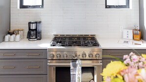Una cocina moderna con estufa de acero inoxidable, dos ventanas y salpicadero de azulejos blancos.