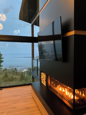 A modern fireplace with a view of the ocean, a flat-screen TV, and a wooden floor.