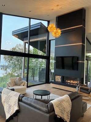 A modern living room with a fireplace, large windows, and a view of the outdoors.