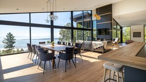 A modern interior with a large dining table, chairs, a bar area, and a view of the sea. - Le Lord, River view, trail and snowmobile (Les Éboulements)