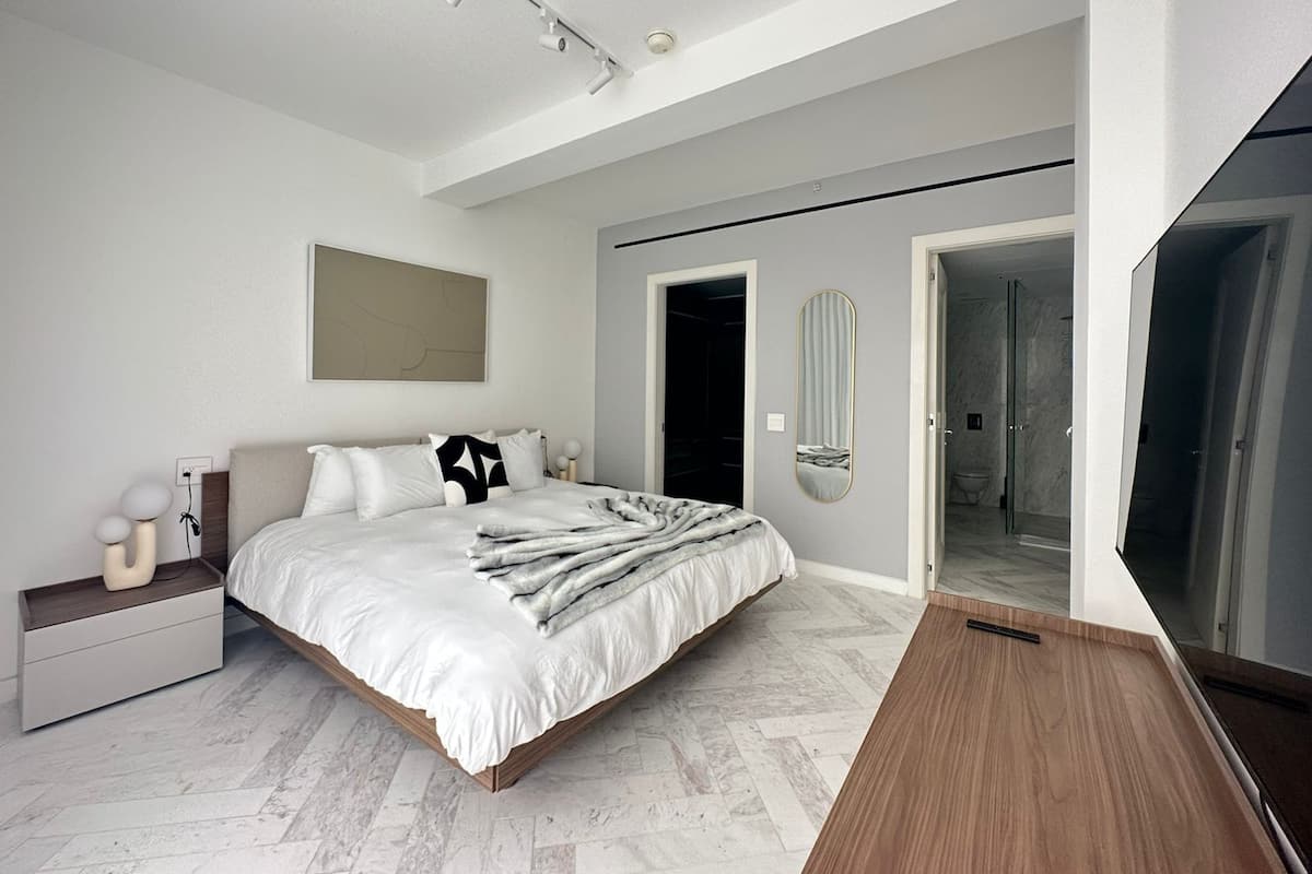 A modern bedroom with a large bed, bedside tables, a mirror, and a walk-in closet.