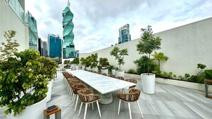 An outdoor terrace with a marble table and wicker chairs, surrounded by potted plants and overlooking a cityscape with modern buildings. - Wanders & Yoo (Panama City)