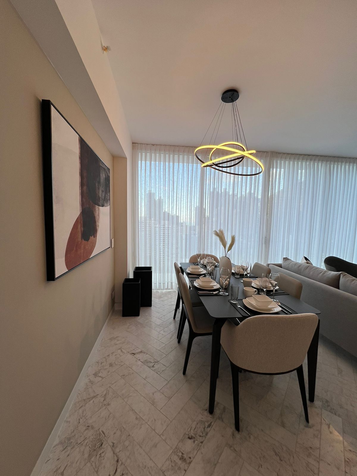 Een moderne eetruimte met een tafel voor vier personen, een bank en een groot raam met dunne gordijnen.