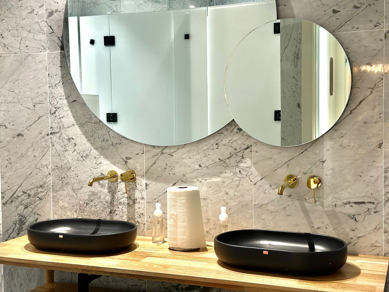 Une salle de bain avec deux lavabos noirs, un miroir et un mur recouvert de carreaux de marbre.