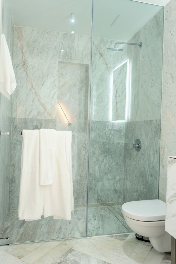 A modern bathroom with a glass-enclosed shower, a white toilet, and a towel rack with two towels. - Wanders & Yoo (Panama City)
