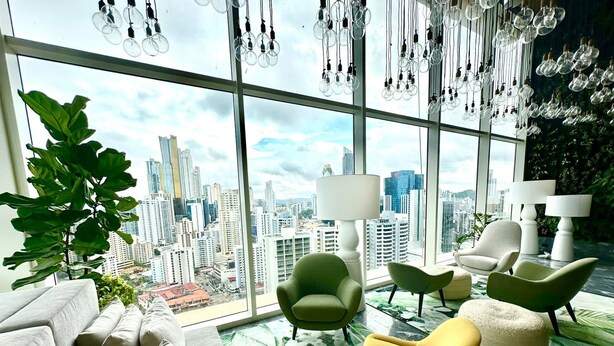 A modern living room with a city view, green chairs, a sofa, and hanging light fixtures. - Wanders & Yoo (Panama City)