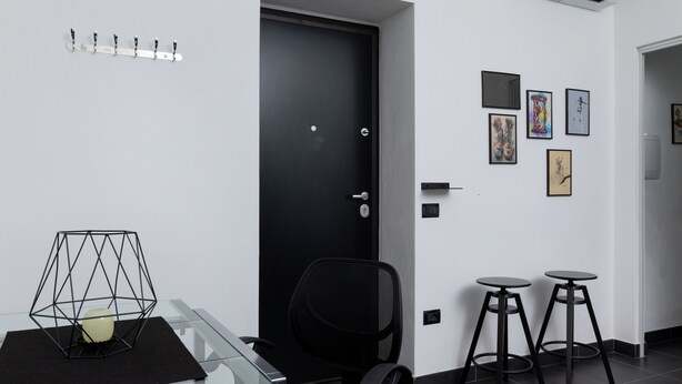 A modern office space with a glass table, a black office chair, two black stools, and a black door. - Bonaventura's House by Wonderful Italy (Olbia)