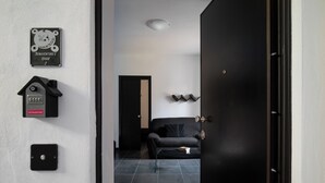 A modern interior with a black door, a black sofa, and a small table with books. There are wall-mounted light switches and a sign above the door. - Bonaventura's House by Wonderful Italy (Olbia)