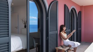 Ein Zimmer mit einem Bett, einer Bank und Blick auf das Meer durch ein Fenster.