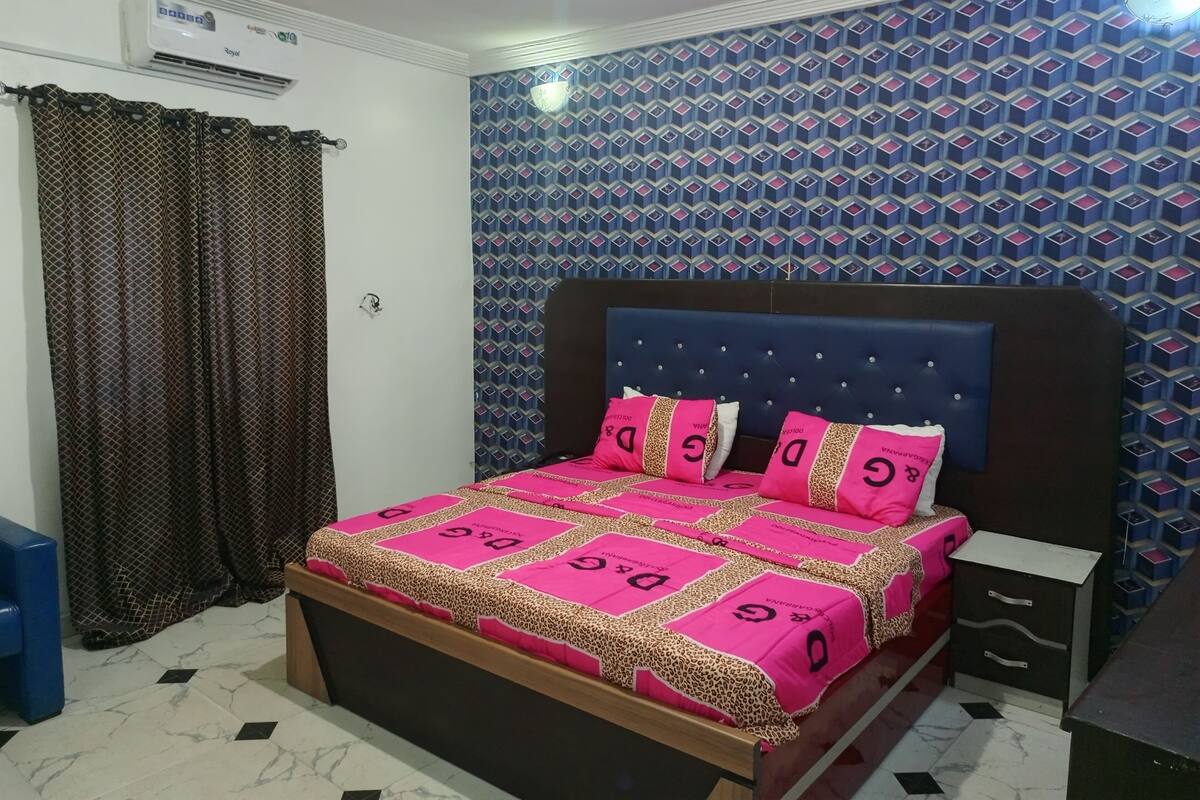 A bedroom with a bed, a nightstand, a wardrobe, and a patterned wall.