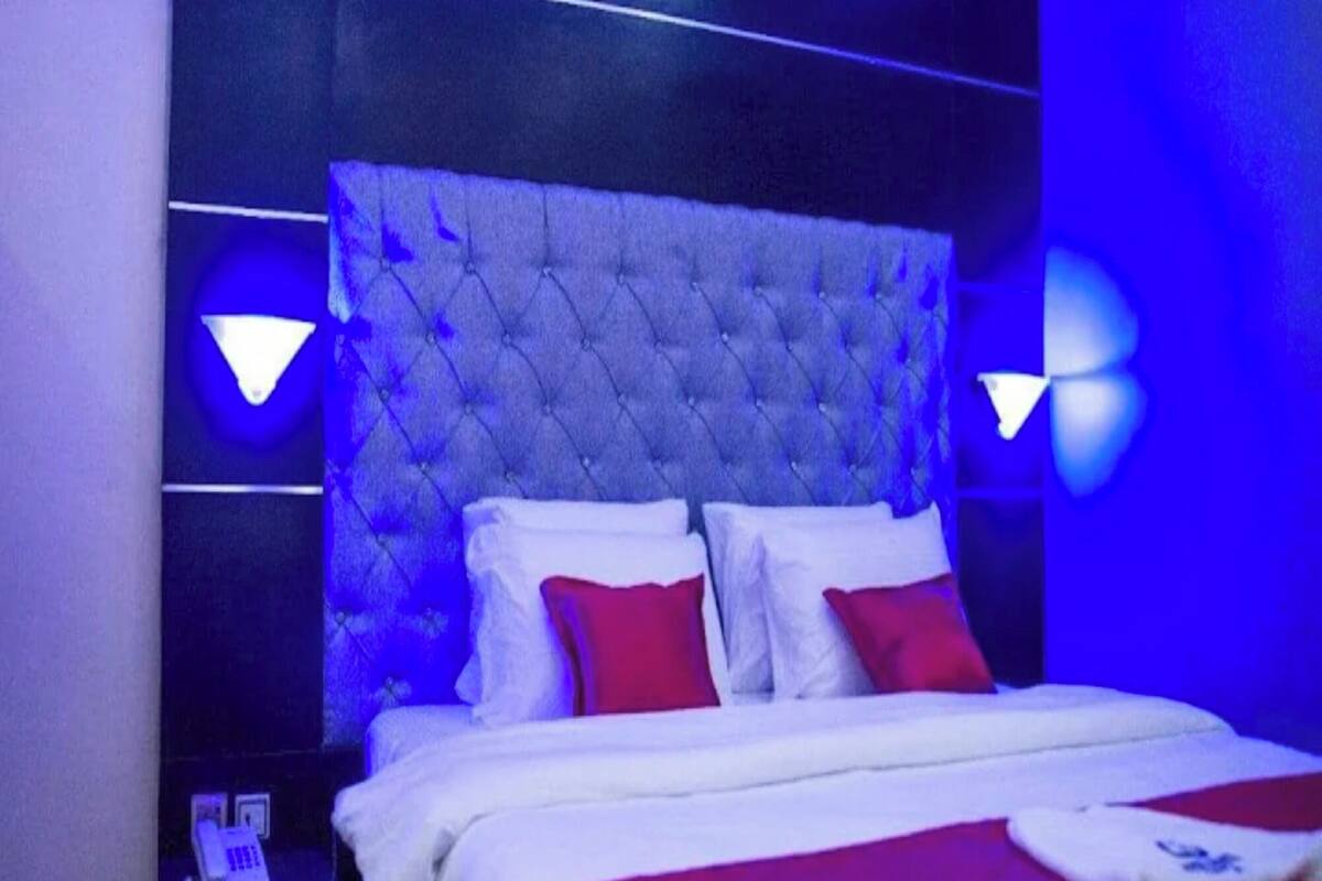 A bedroom with a tufted headboard, white bedding, red pillows, and two wall-mounted lamps.