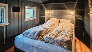 Ein Doppelbett mit zwei Kissen, ein Fenster mit Blick auf Grünflächen und Wandleuchten.
