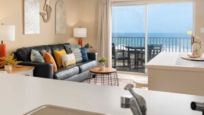 A modern living room with a black leather sofa, colorful cushions, a wooden coffee table, and a view of the ocean through large sliding doors. - Stylish Beachfront Retreat ~ Gulf Views ~ Pools! (Orange Beach)