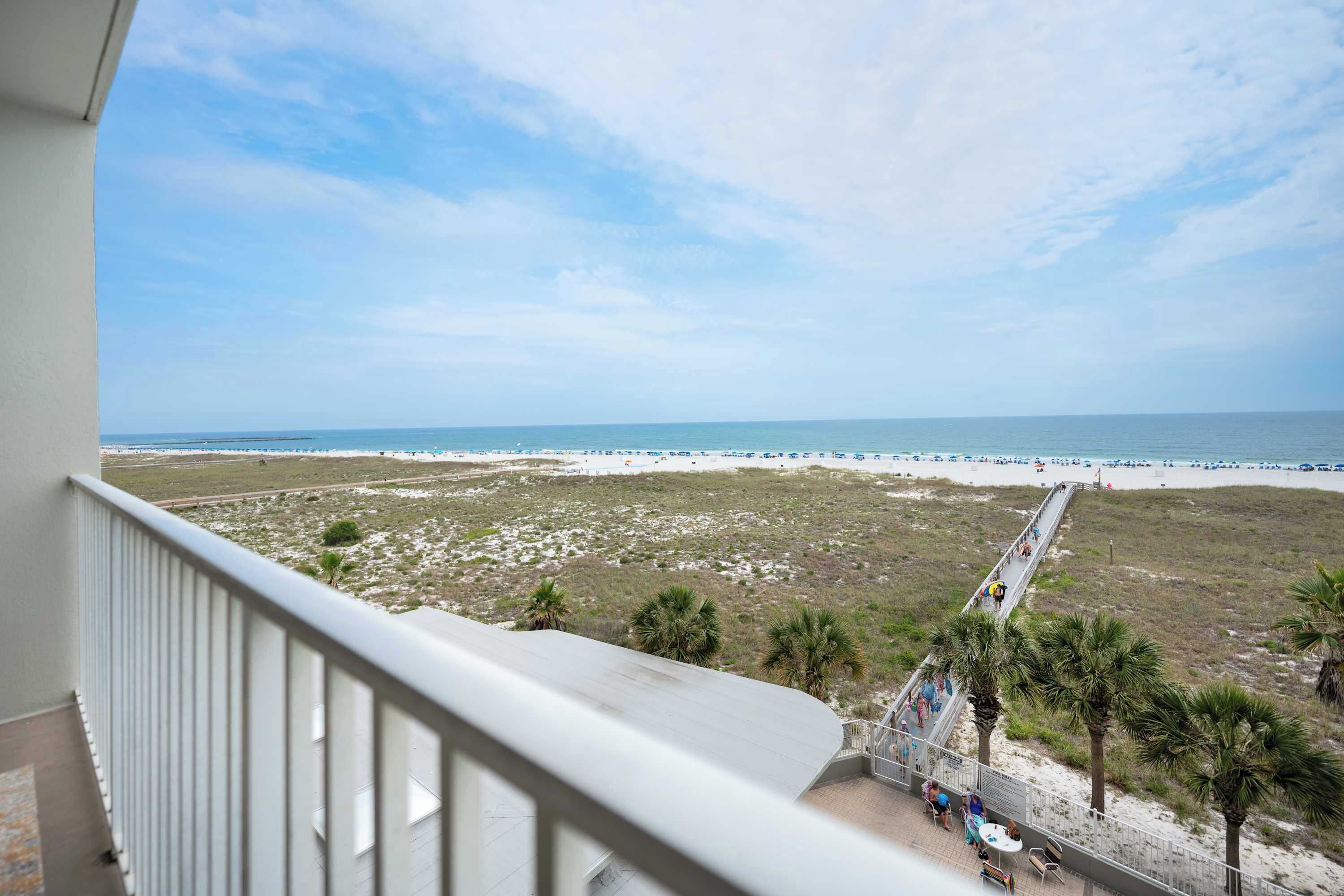 Een balkon met uitzicht op een strand, een promenade en palmbomen.