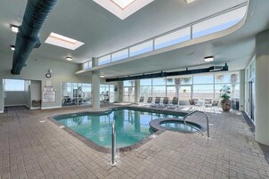 Piscina interna com claraboia, equipamentos de ginástica e cadeiras de descanso.