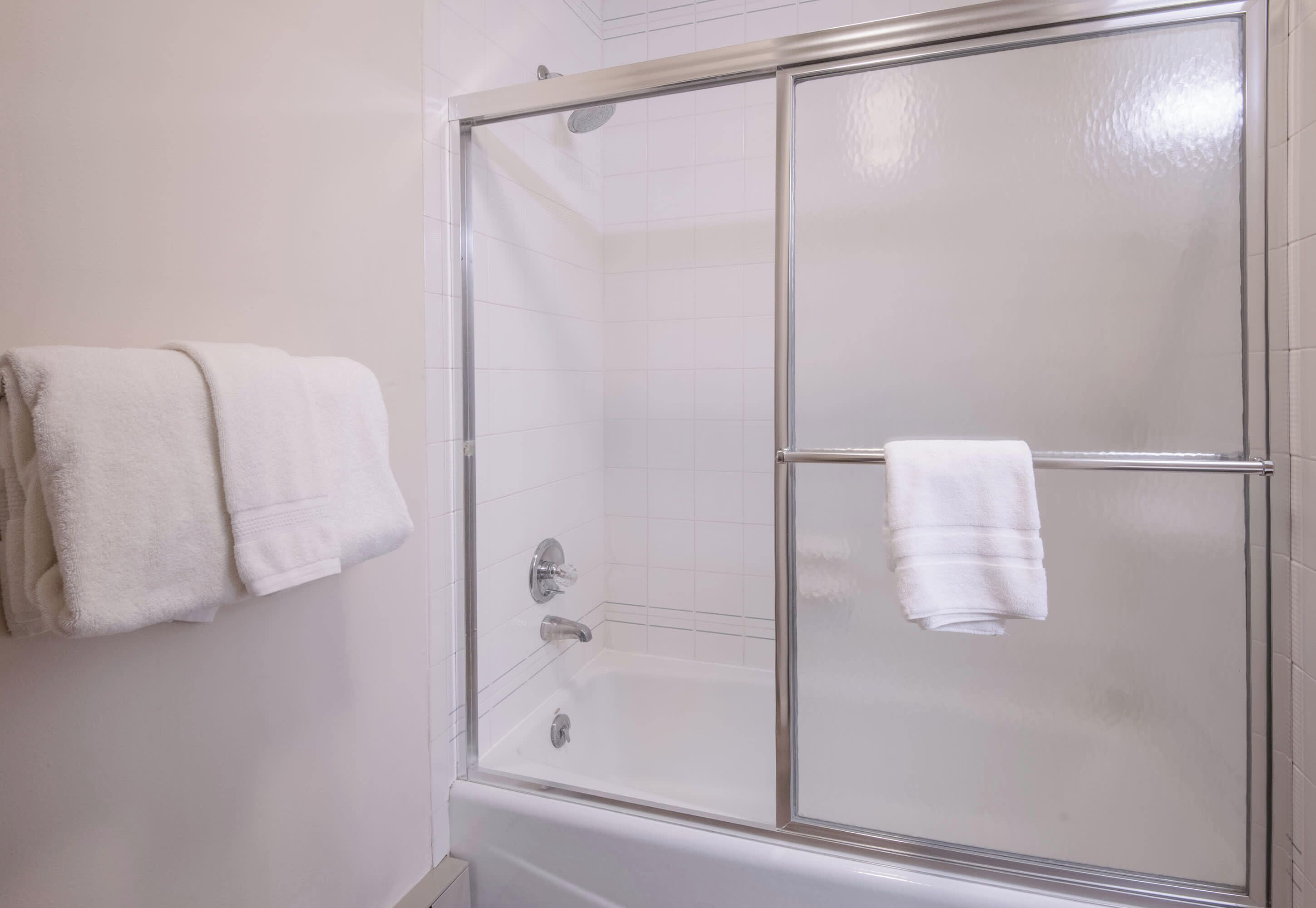 Une douche fermée par des parois de verre, avec une baignoire blanche et des serviettes assorties.