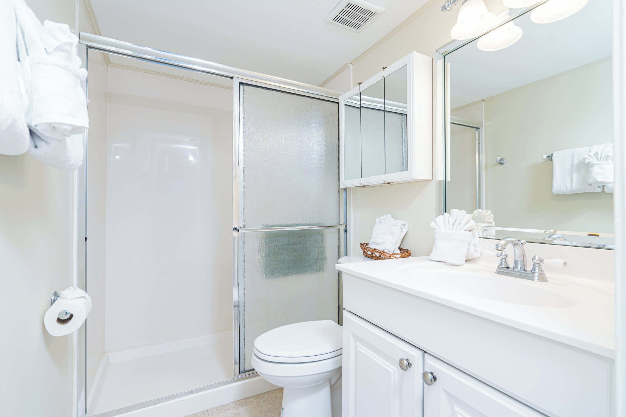 A bathroom with a glass shower enclosure, a white toilet, a sink with a mirror, and a towel rack.