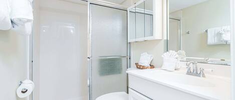 A bathroom with a glass shower enclosure, a white toilet, a sink with a mirror, and a towel rack.