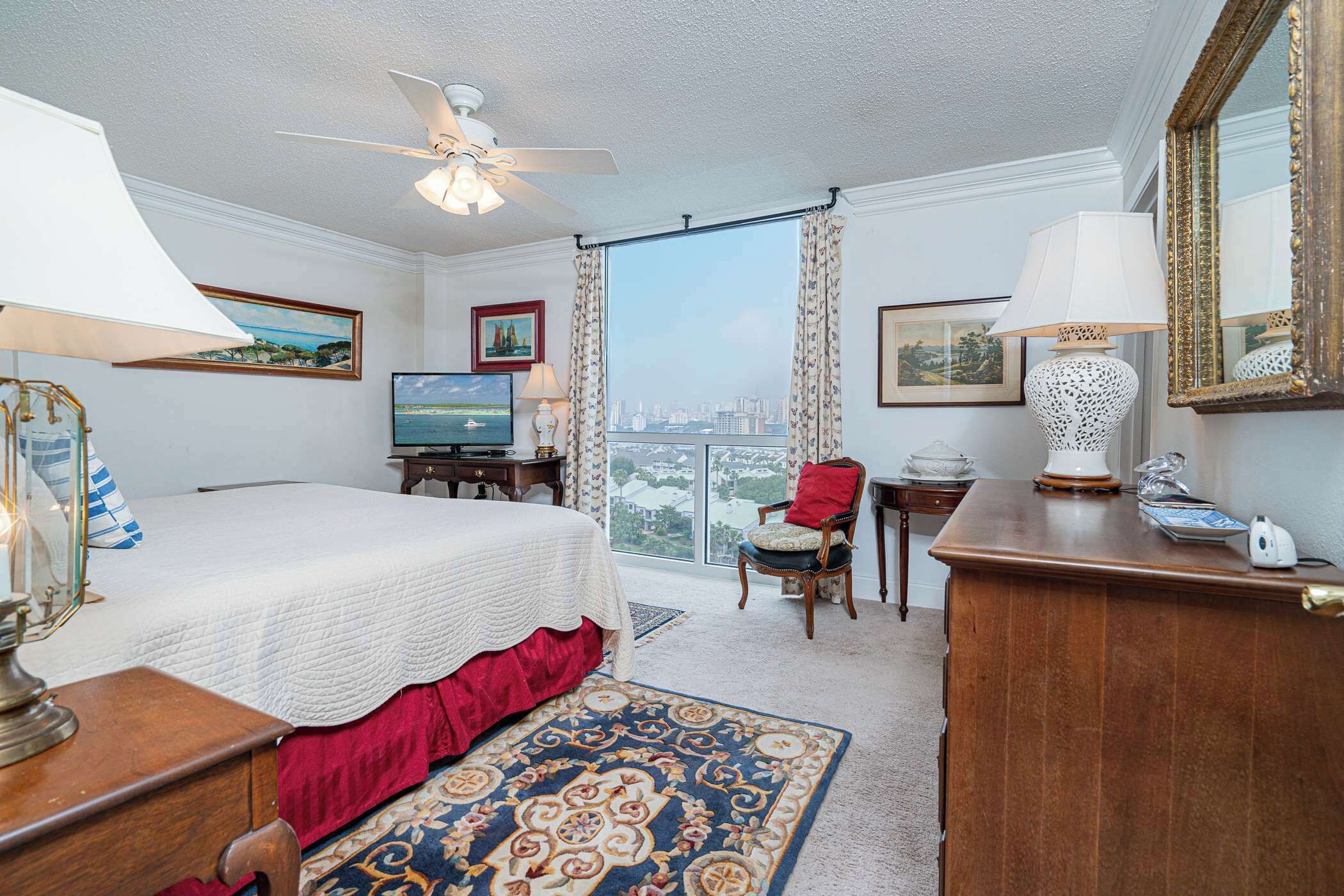 A hotel room with a bed, a desk, a chair, a television, and a view of the city.