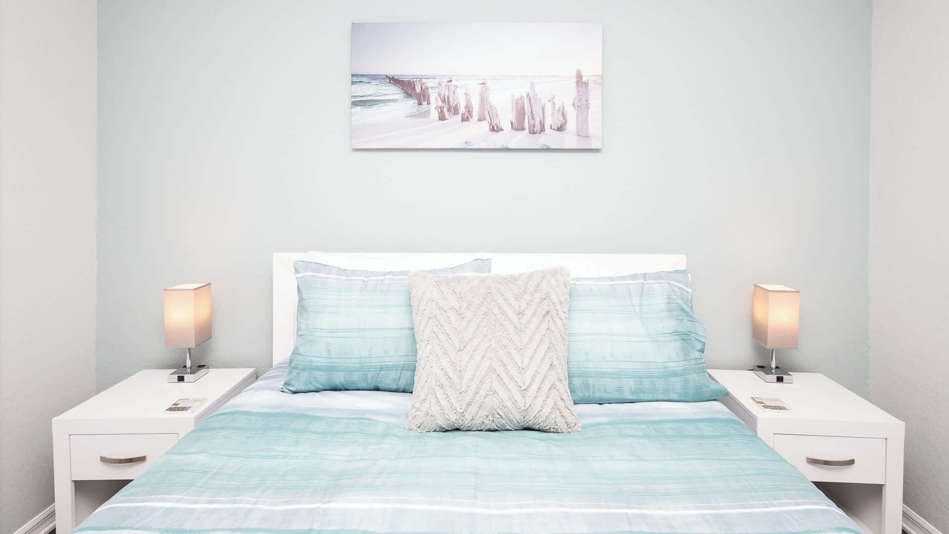A bedroom with a bed, two bedside tables, and a wall-mounted picture.
