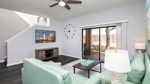 A living room with a staircase, a television, a clock, and a view of the outdoors. - Just Beachy at Regal Palms (Davenport)