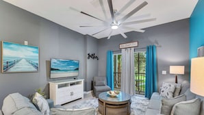 A modern living room with a ceiling fan, a flat-screen TV, a white cabinet, grey sofas, and a coffee table. - Oasis Hideaway @bahama Bay (Davenport)