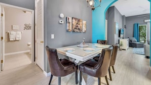 A dining area with a white table, brown chairs, and a chandelier. There is a painting on the wall and a small plant on the table. - Oasis Hideaway @bahama Bay (Davenport)