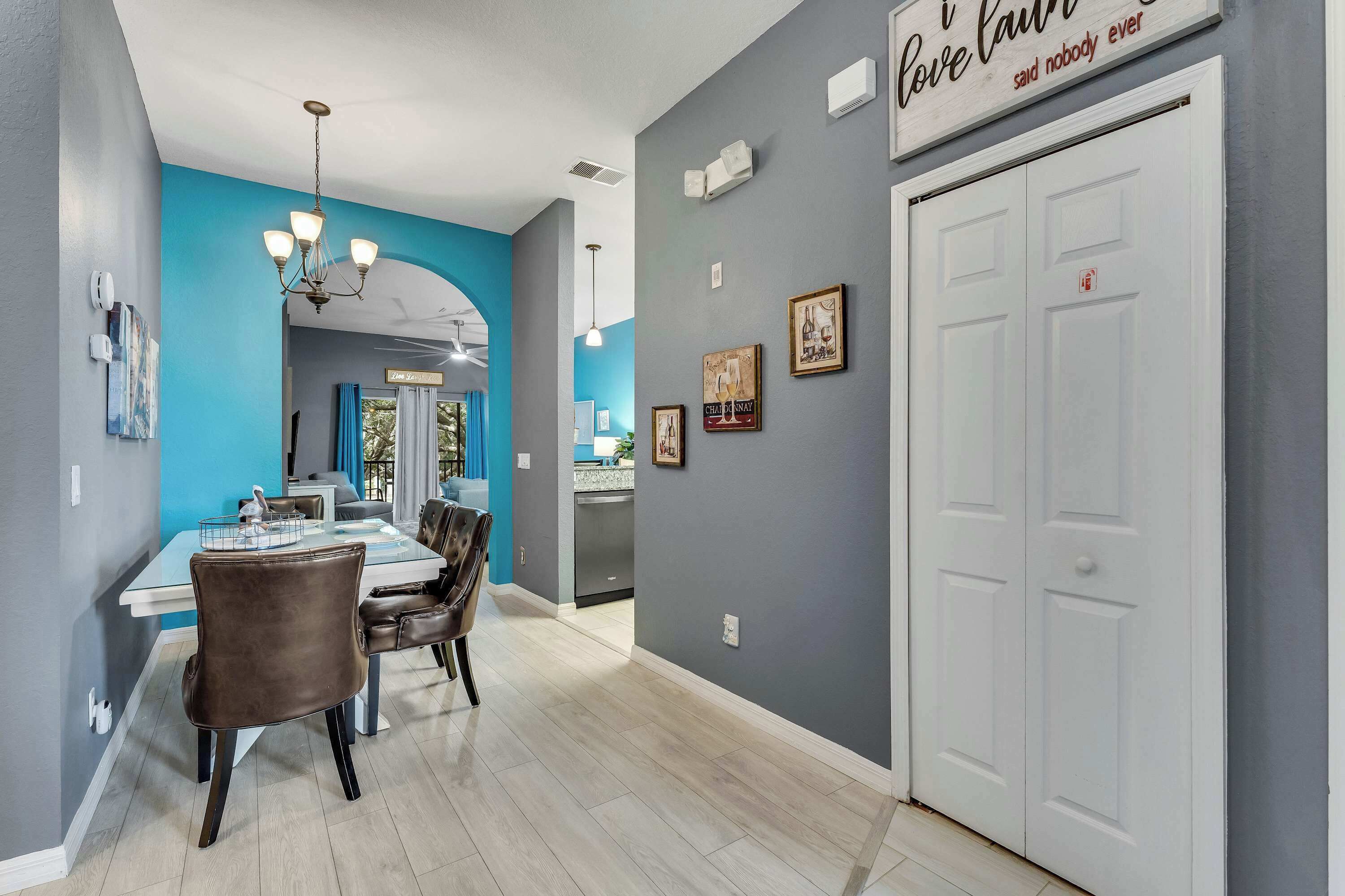 A modern dining area with a blue accent wall, a chandelier, and a white door with a sign above it.