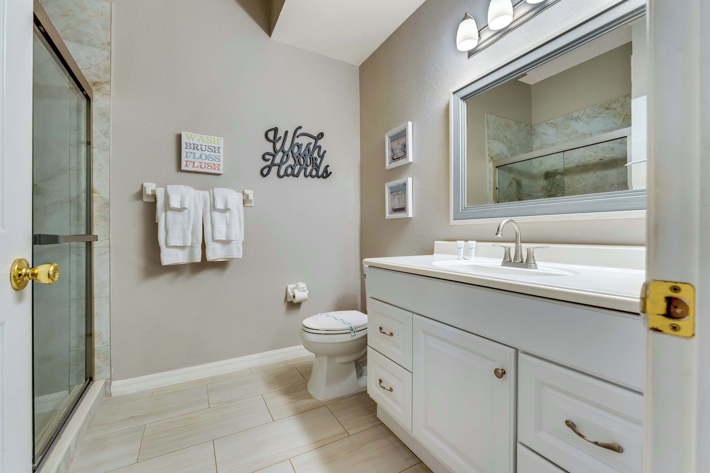 A bathroom with a toilet, sink, and a mirror. There are towels hanging on the wall and a sign that says 'Wash Your Hands'.
