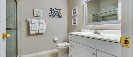 A bathroom with a toilet, sink, and a mirror. There are towels hanging on the wall and a sign that says 'Wash Your Hands'.
